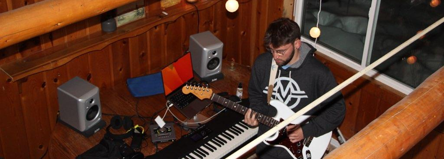 Music studio with wooden walls, string lights, and a musician playing guitar and keyboard